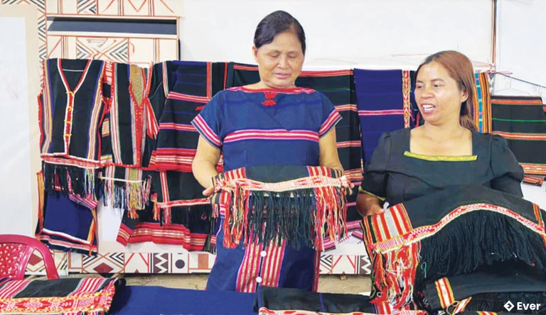 Bà Kpă H’Uyên (bìa trái) giới thiệu sản phẩm dệt thổ cẩm của chị em trong làng tới du khách